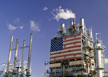 Part of oil refinery complex with big american flag displayed. Fumes coming out from the chimney.