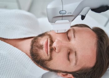 Bearded mustached dark-haired man dozing during a non-invasive face-lift procedure