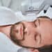 Bearded mustached dark-haired man dozing during a non-invasive face-lift procedure