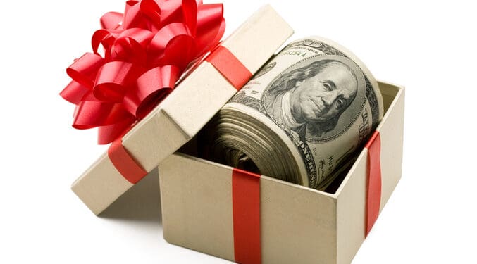A roll of hundred dollar bills laying in a gift box that is decorated with red bow.