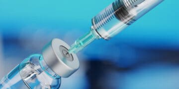 Medical disposable syringe for vaccine injection and glass vial on blue blur background.